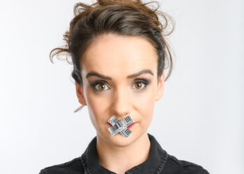A photo of comedian Gabby Killick, she has her dark hair in an undo and has silver tape in a cross over her mouth
