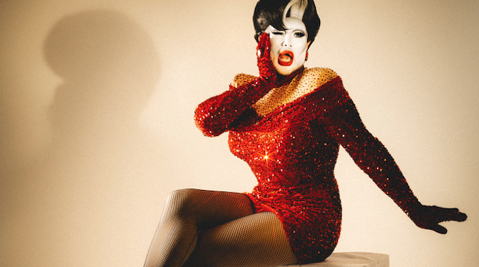 Singer and drag star Danny Beard sits in a studio wearing a red sequin dress