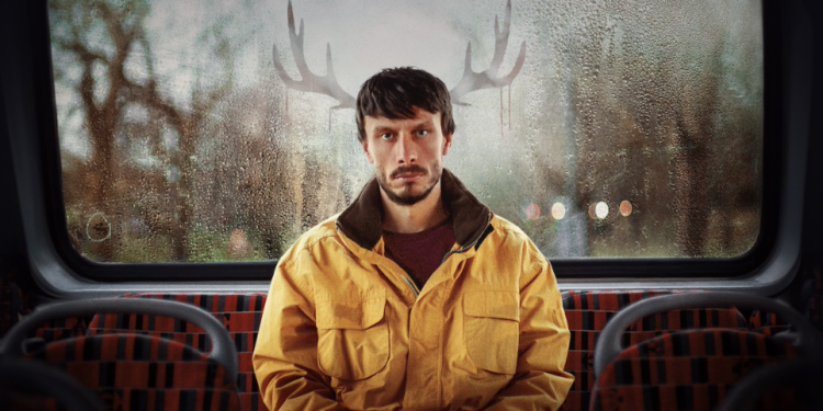 Richard Gadd as Donny Dunn, he is sat at the back of a bus wearing a yellow jacket, the condensation on the bus window is shaped like antlers