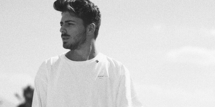 A black and white photo of a young man wearing a white t shirt looking off camera