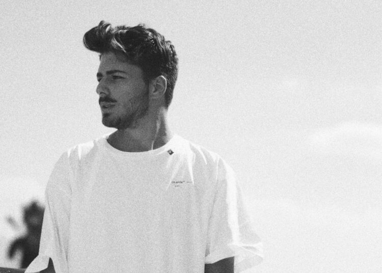 A black and white photo of a young man wearing a white t shirt looking off camera