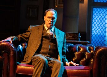 Actor Todd Boyce sits on a oxblood leather Chesterfield sofa wearing a tweed 3 piece suit