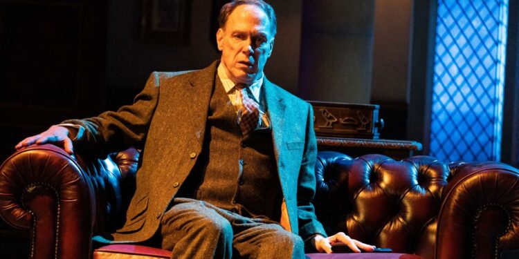 Actor Todd Boyce sits on a oxblood leather Chesterfield sofa wearing a tweed 3 piece suit