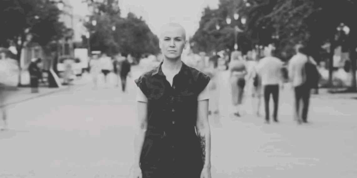 Black-and-white image of a woman standing still on a busy pedestrian street, with blurred people moving around her and the text “Time Stands Still – Gitika Partington” overlaid.