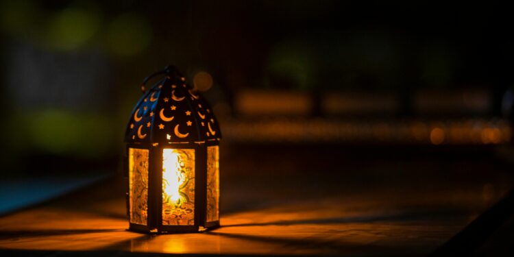 Glowing lantern with crescent moon and star cut-outs casting warm light in a dark setting.